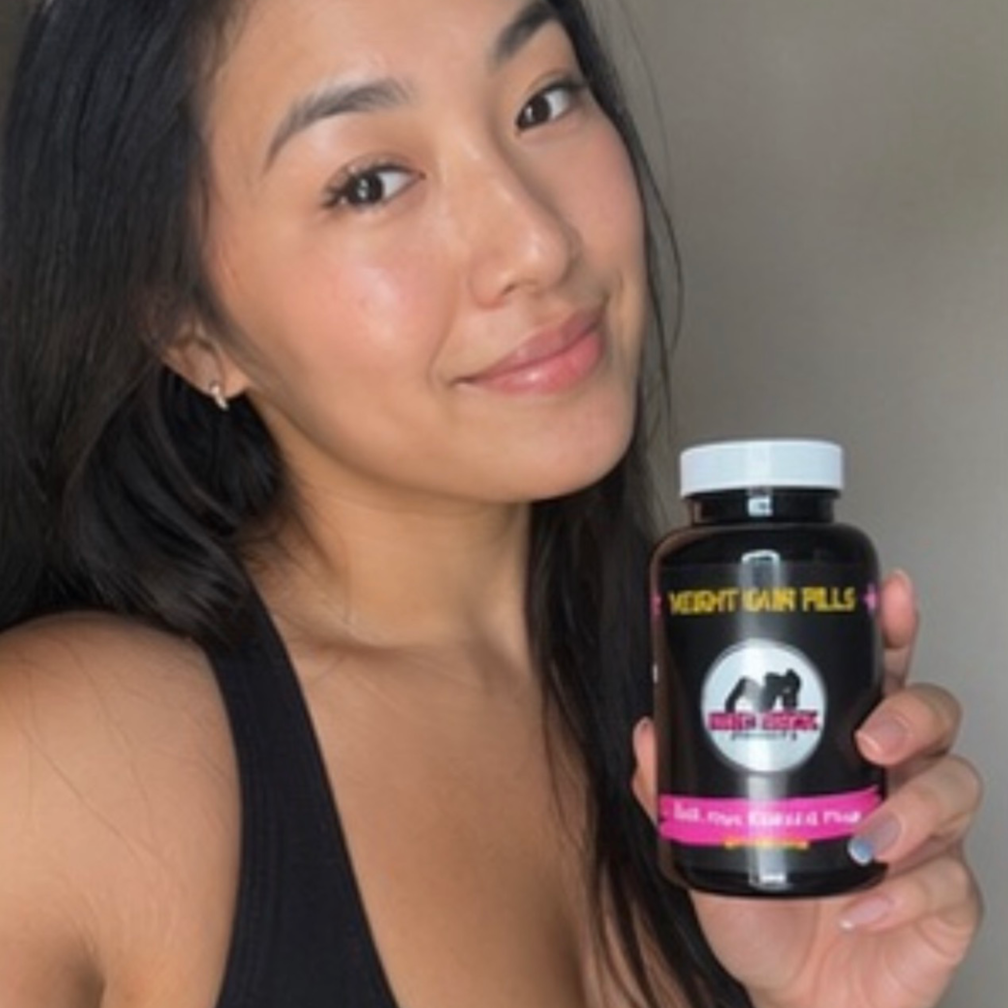 Woman holding a supplement bottle labeled 'Weight Gain Pills' against a neutral background
