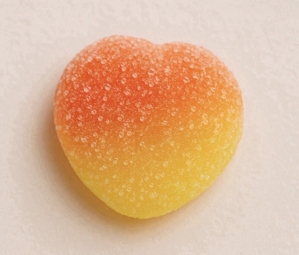 Heart-shaped gummy candy with a gradient of orange to yellow on a beige background
